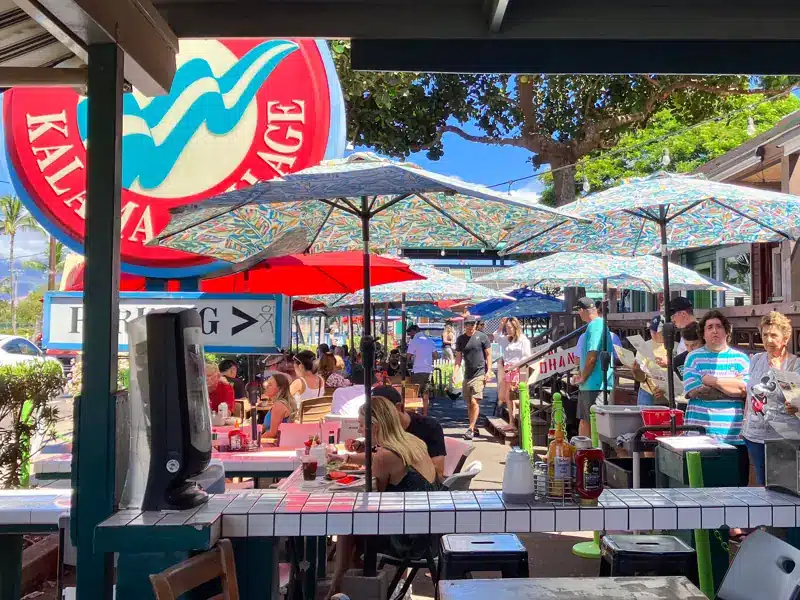 Diners at outdoor tables under colorful umbrellas at Kihei Caffe in Kalama Village, Kihei, Maui