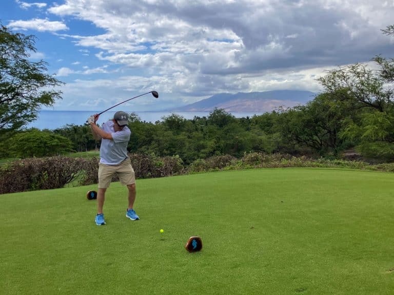 Golfer teeing off at a Wailea golf course with the ocean and West Maui Mountains behind