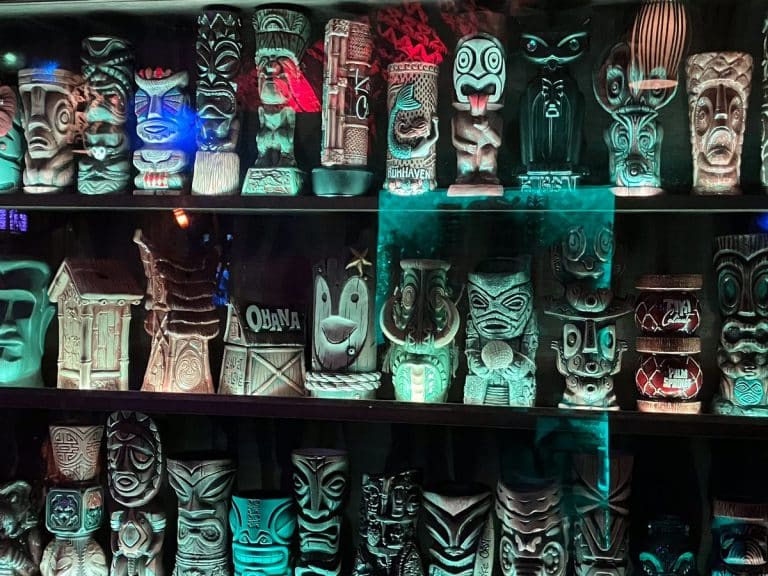 Shelves of collectible tiki mugs glowing behind a tiki bar