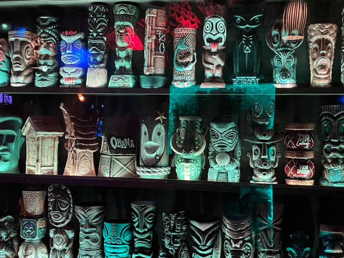 Shelves of collectible tiki mugs glowing behind a tiki bar